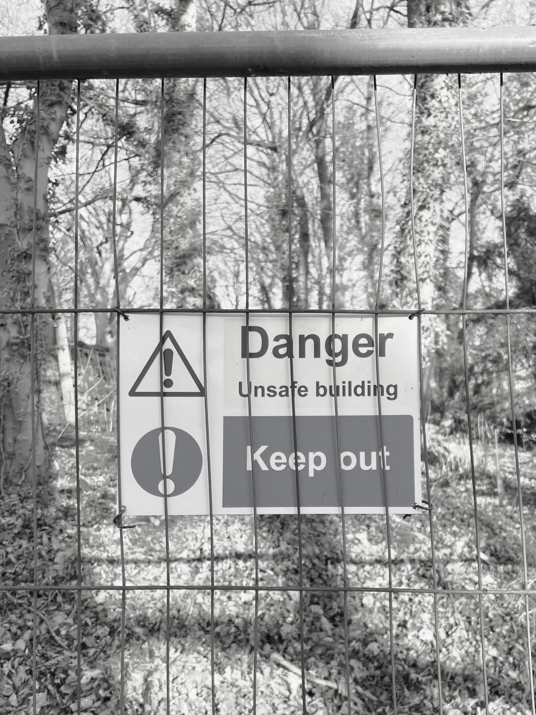Danger, unsafe building, keep out — warning signs wired to the fence that seals the ruins off.