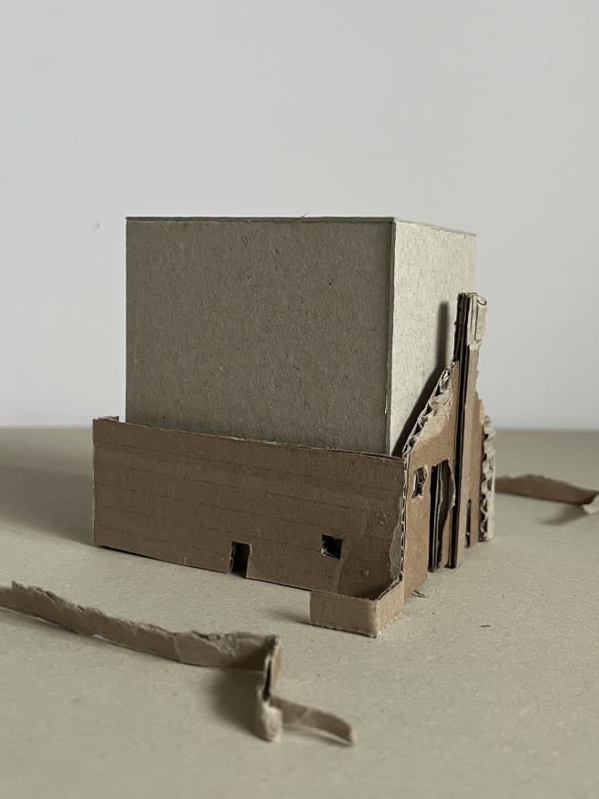 Cardboard study model — a solid new volume seated on the ruin wall.