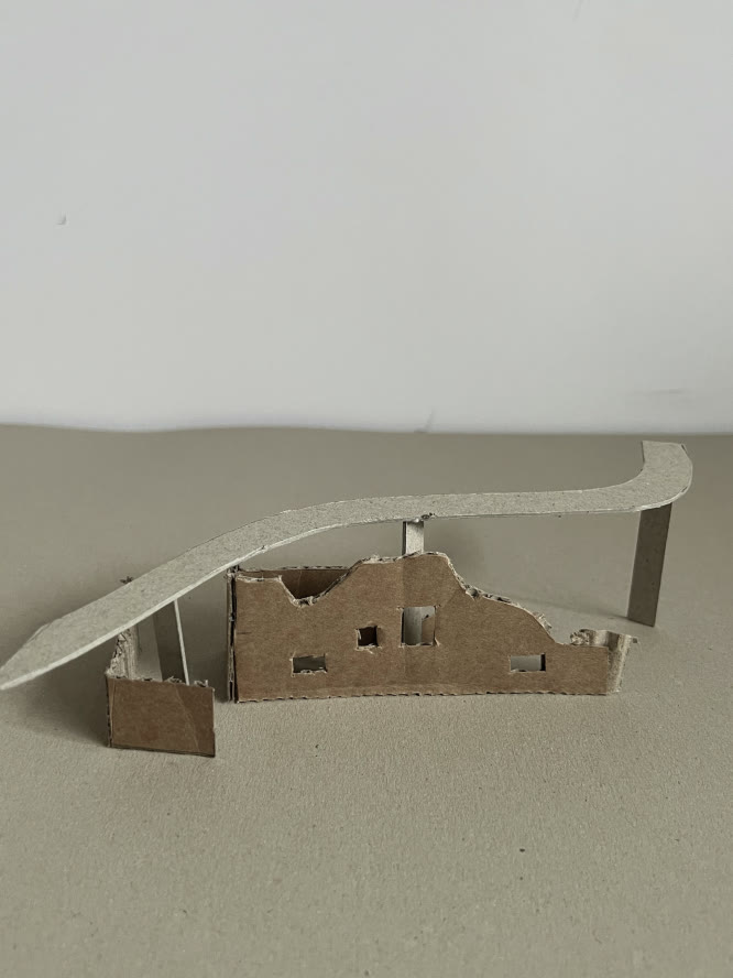 Cardboard study model — a leaning roof plane sheltering the fragments.